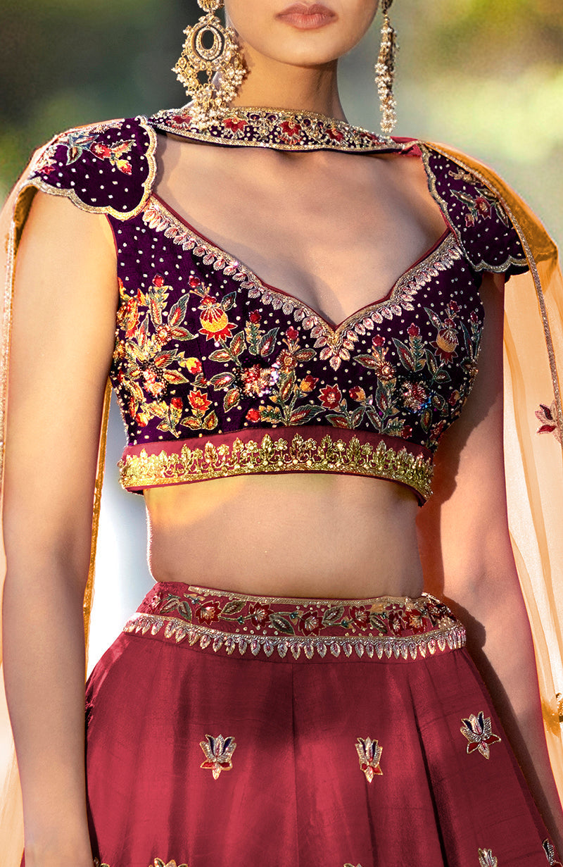 A woman models a brick red and aubergine lehenga set with intricate embroidery.