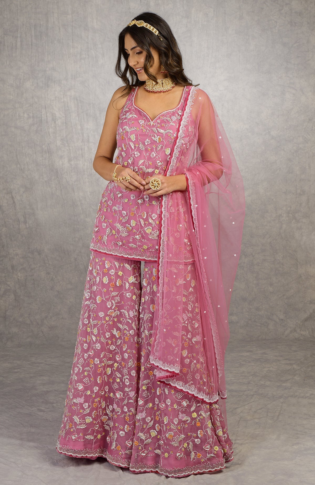 A woman in a violet sharara set with floral embroidery and a sheer dupatta.