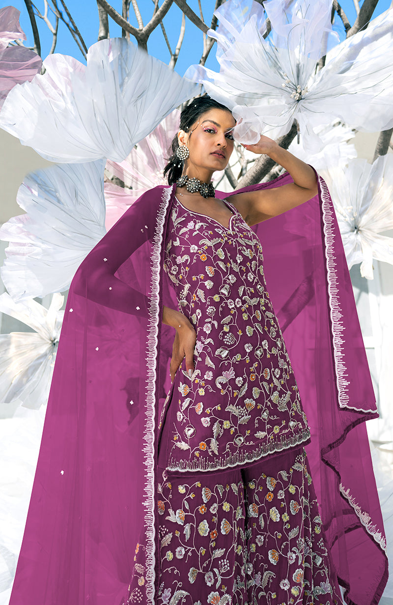 A woman models a raspberry sharara set with intricate floral embroidery.