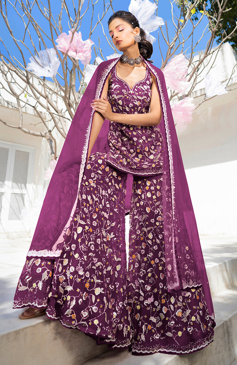 A woman models a raspberry sharara set with floral embroidery and a sheer dupatta.