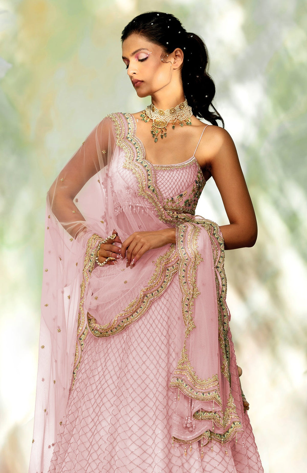 A model poses in a pink lehenga set with intricate gold and green embroidery.