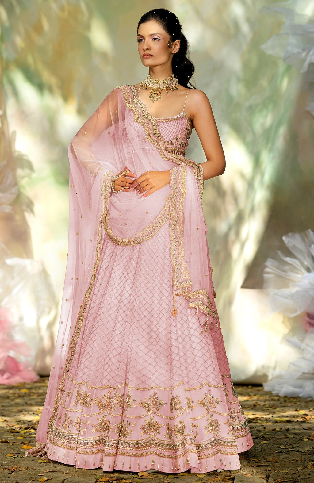 A model poses in a pink lehenga set with gold embroidery and a matching dupatta.