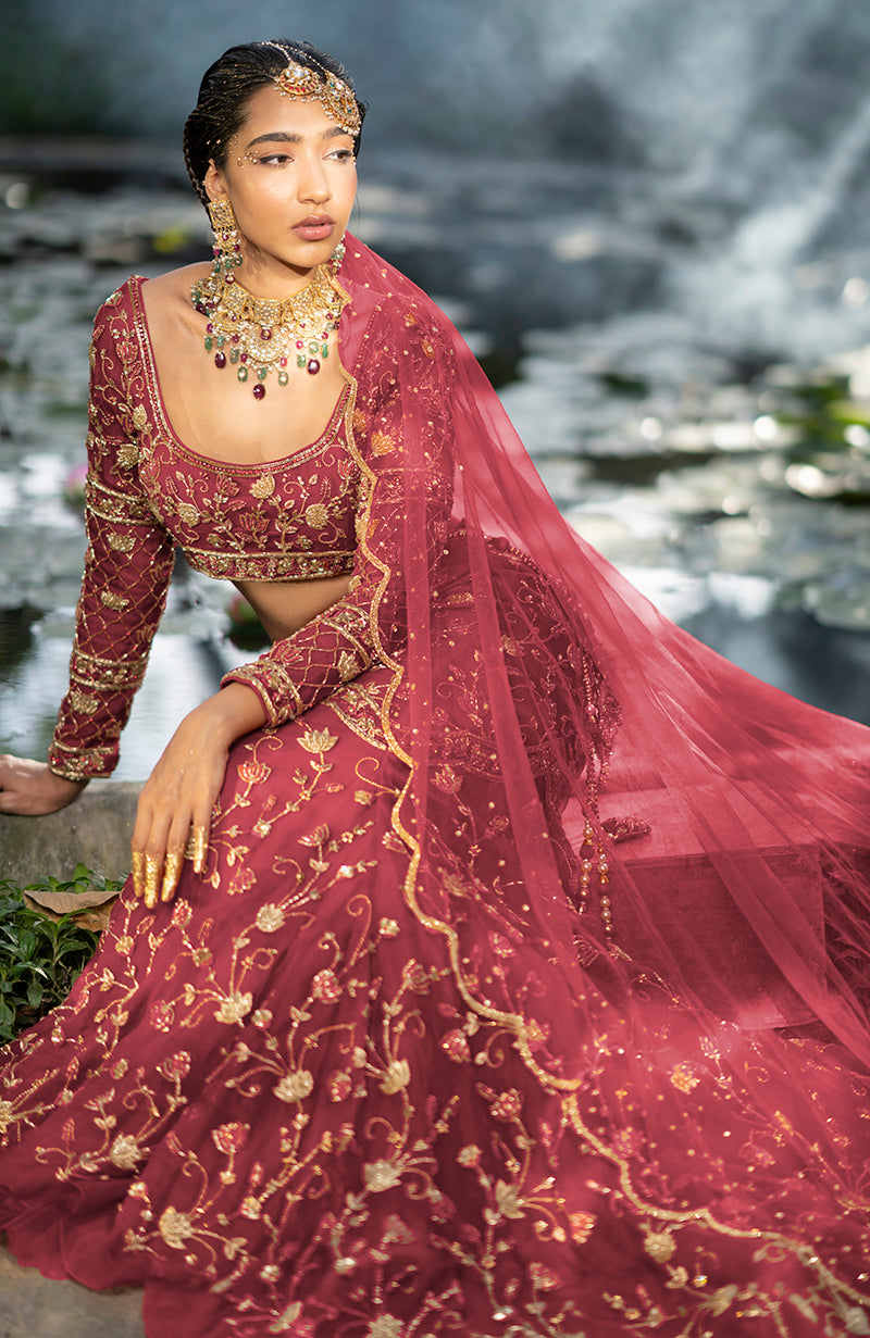 A model in a peacock pink lehenga set with gold embroidery and jewelry.