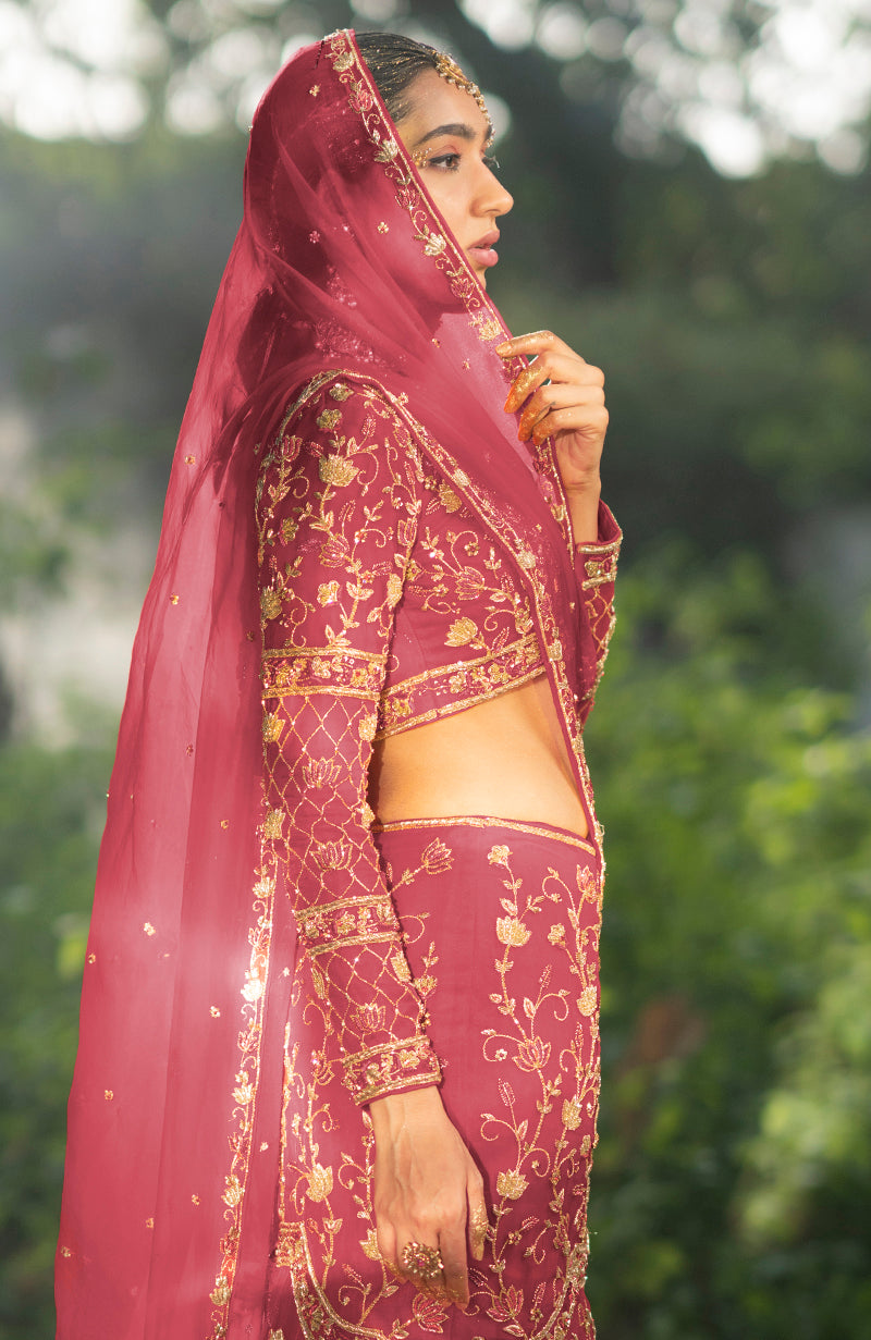 A woman in a deep rosewood lehenga set with gold embroidery and a sheer dupatta.