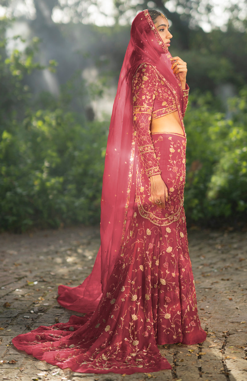 A woman in a deep rosewood lehenga set with gold embroidery and a flowing train.