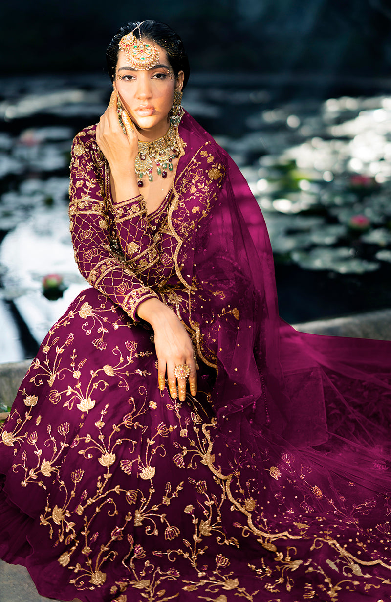 A woman models a peacock pink lehenga set with gold embroidery and jewelry.