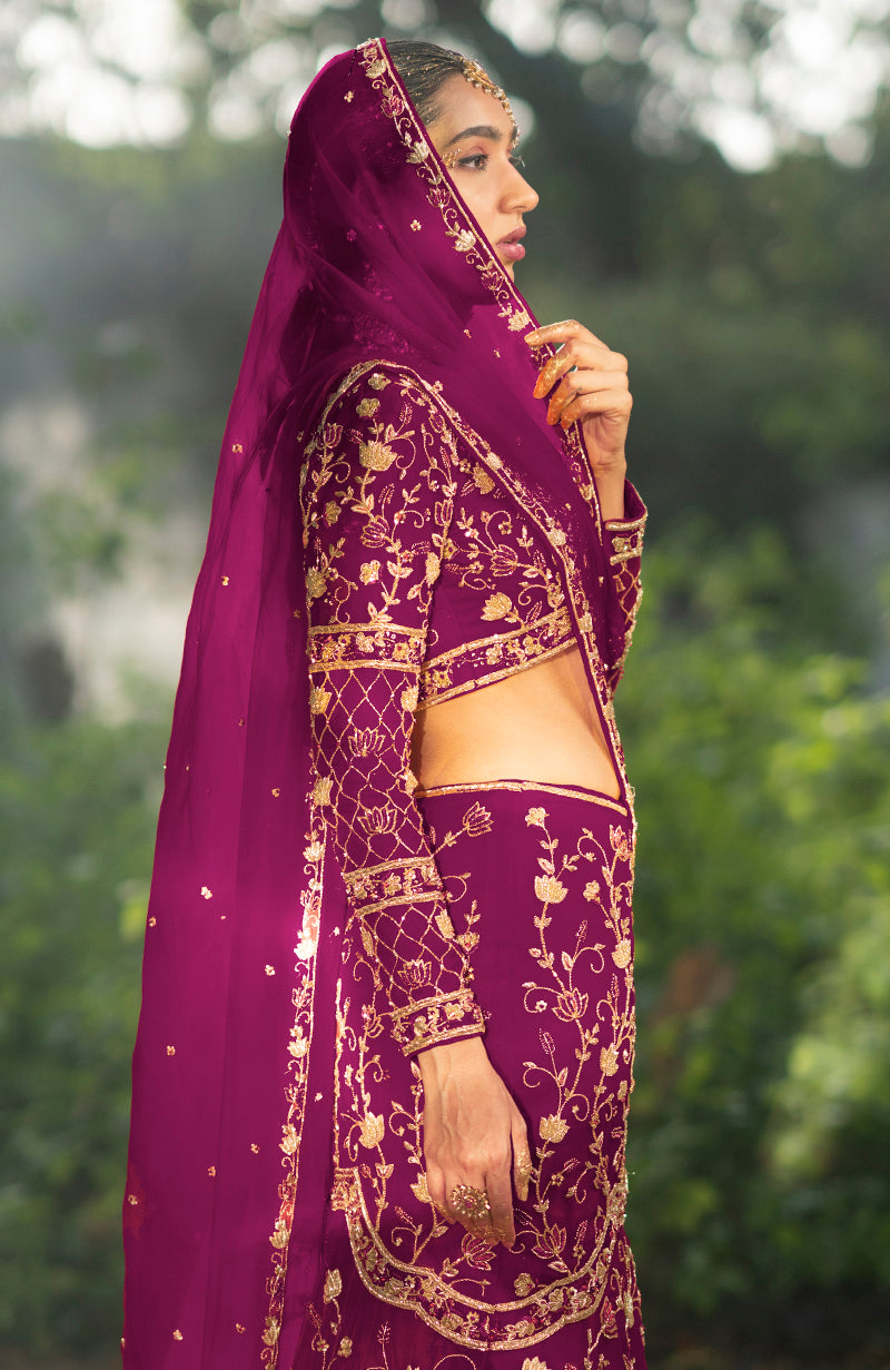 A woman in a peacock pink lehenga set with gold embroidery and a matching dupatta.