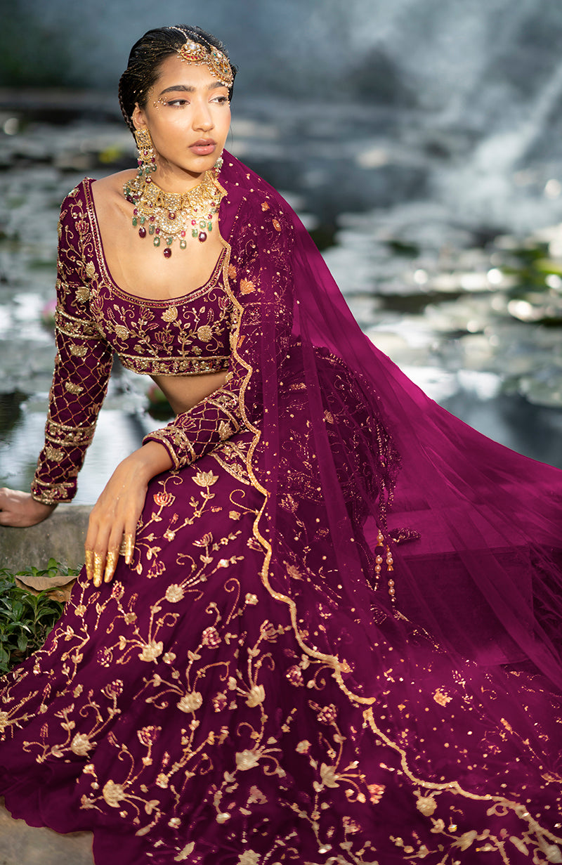A woman in a pink lehenga set with gold embroidery sits by a pond.