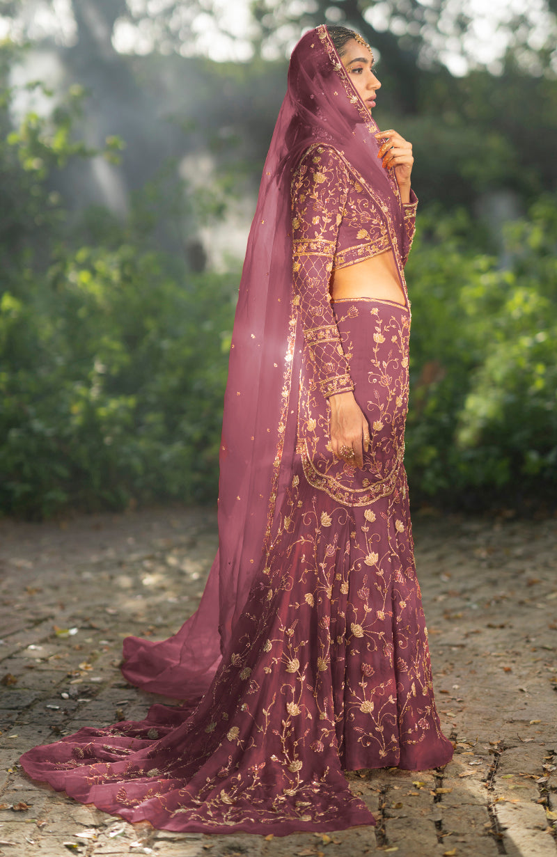 A woman in a rose wine lehenga set with gold embroidery and a sheer dupatta.
