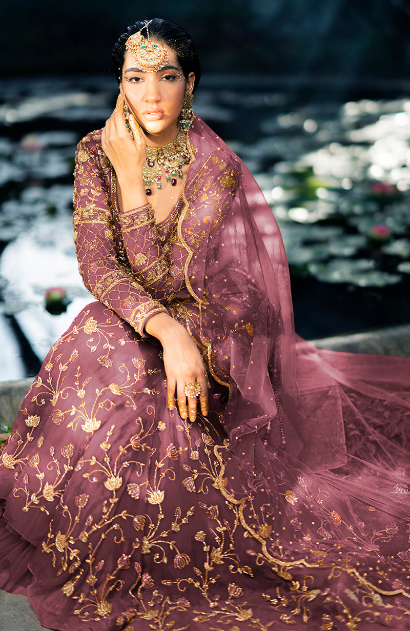 A woman models a rose wine lehenga set with gold embroidery and a sheer dupatta.