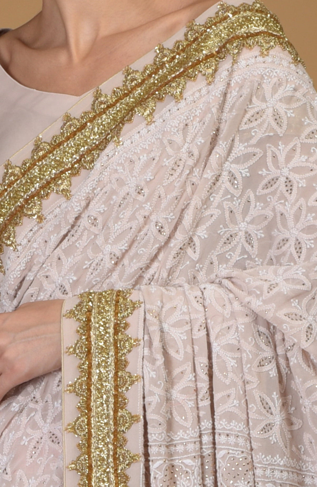 Nude pink Georgette saree with hand-embroidered Chikankari and gold zardozi details.
