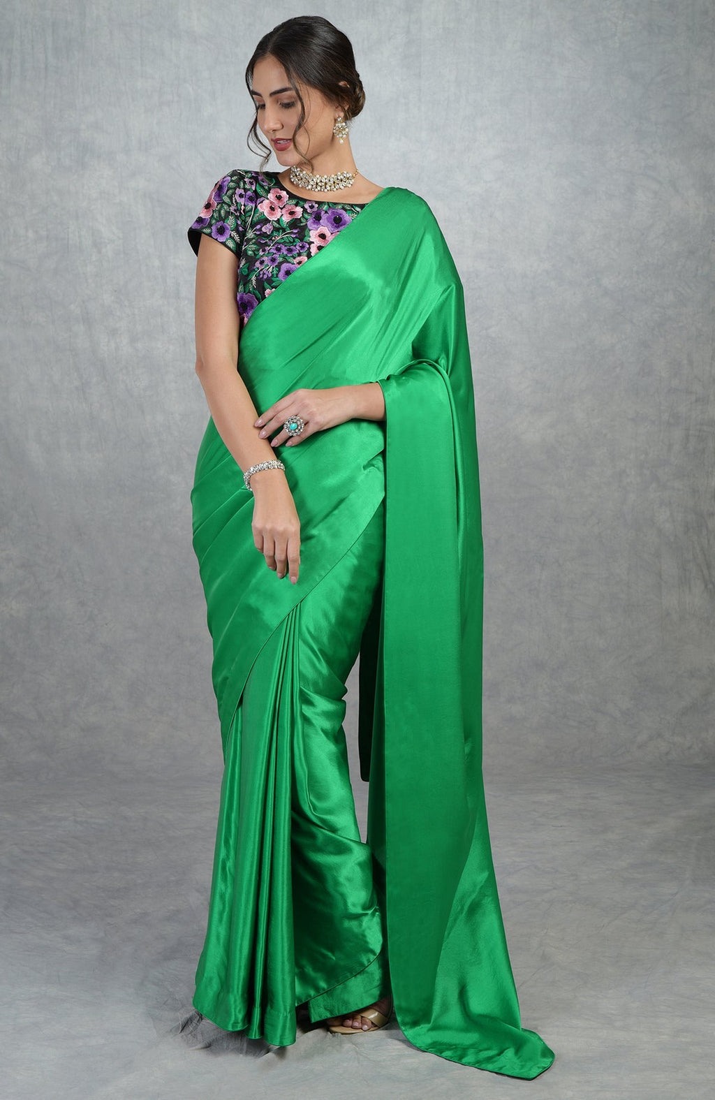 Emerald green satin silk saree with black satin blouse featuring multicolor floral embroidery.