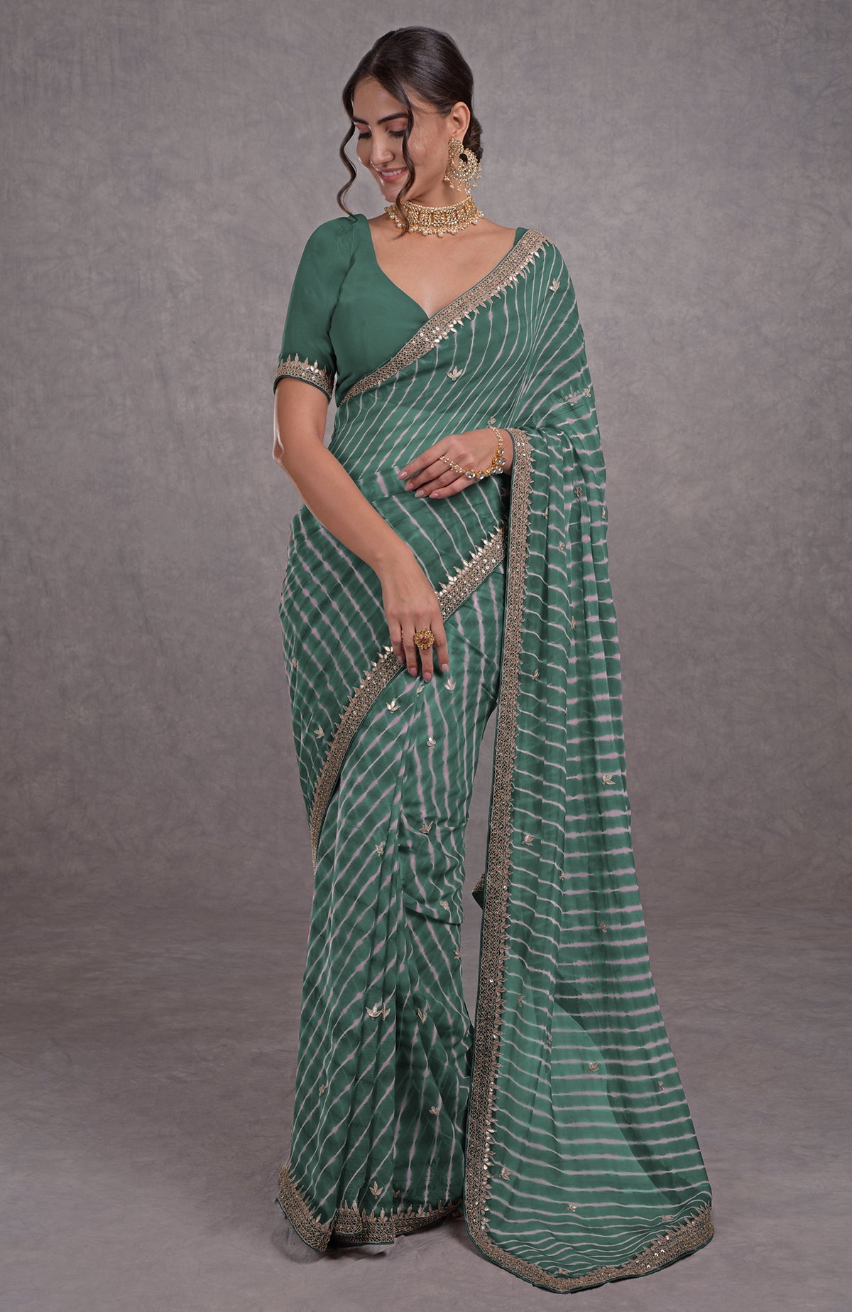 A woman in a green leheriya saree with rose gold embroidery and a matching blouse.
