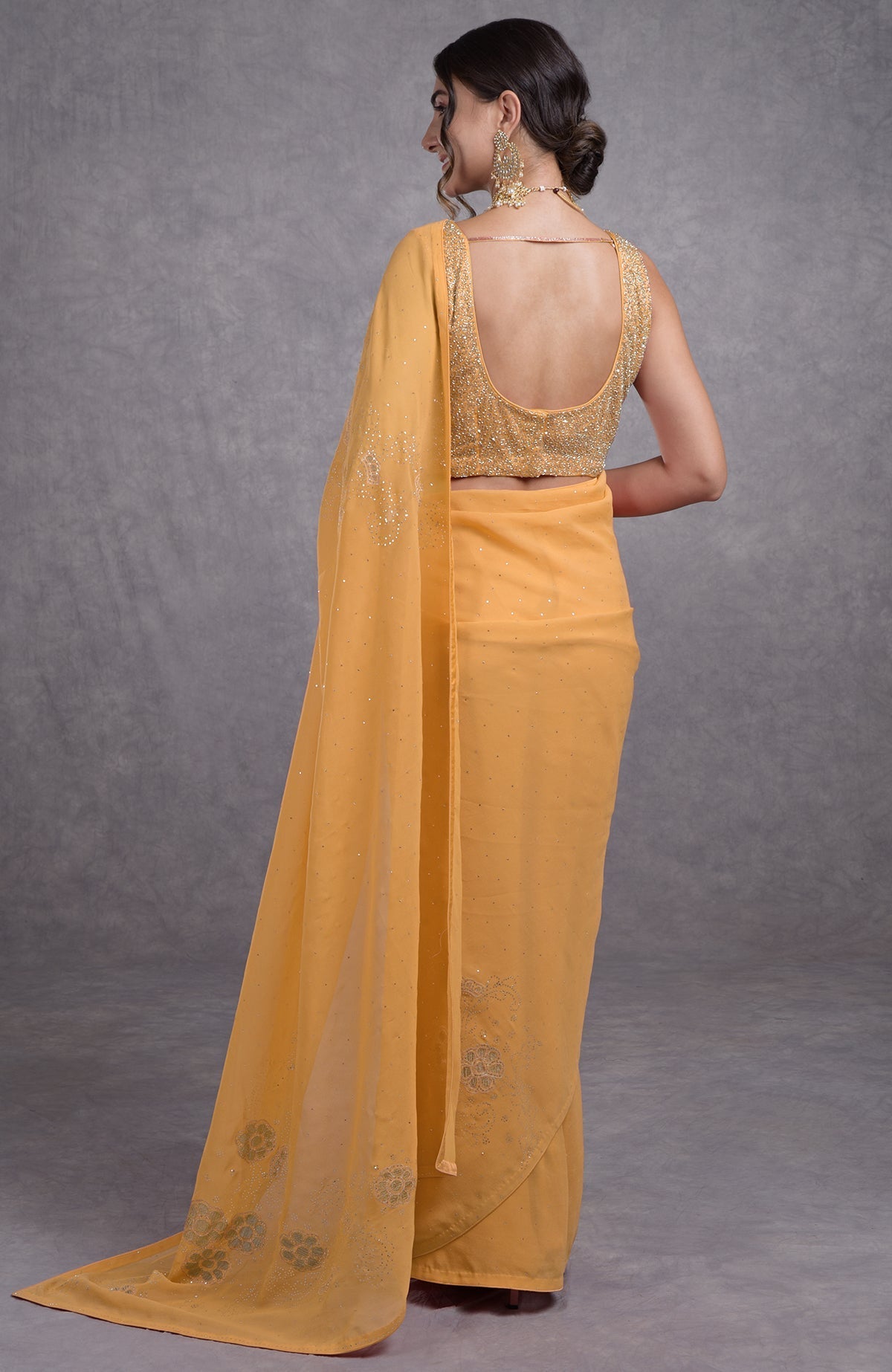 A woman models a buff yellow saree with a gold embroidered blouse from the back.