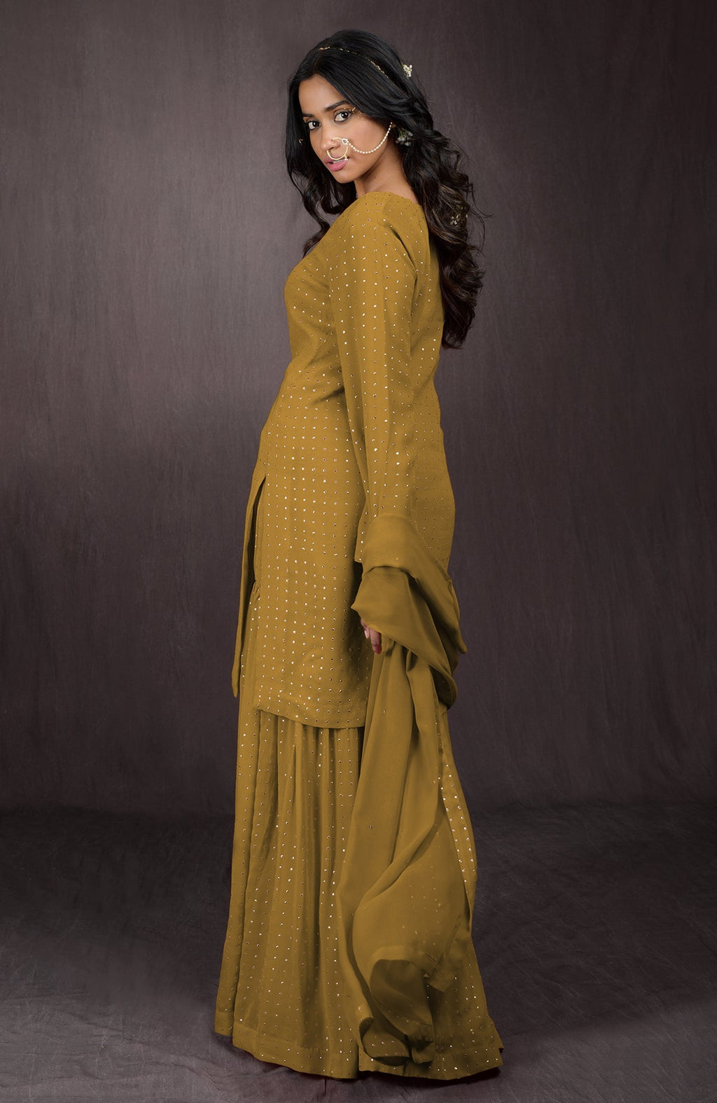 A woman models a mustard yellow sharara set with gold embellishments.