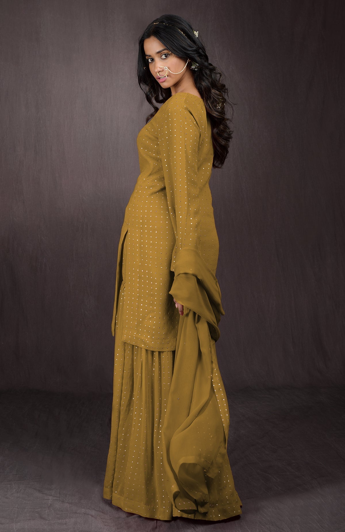 A woman models a mustard yellow sharara set with gold embellishments.