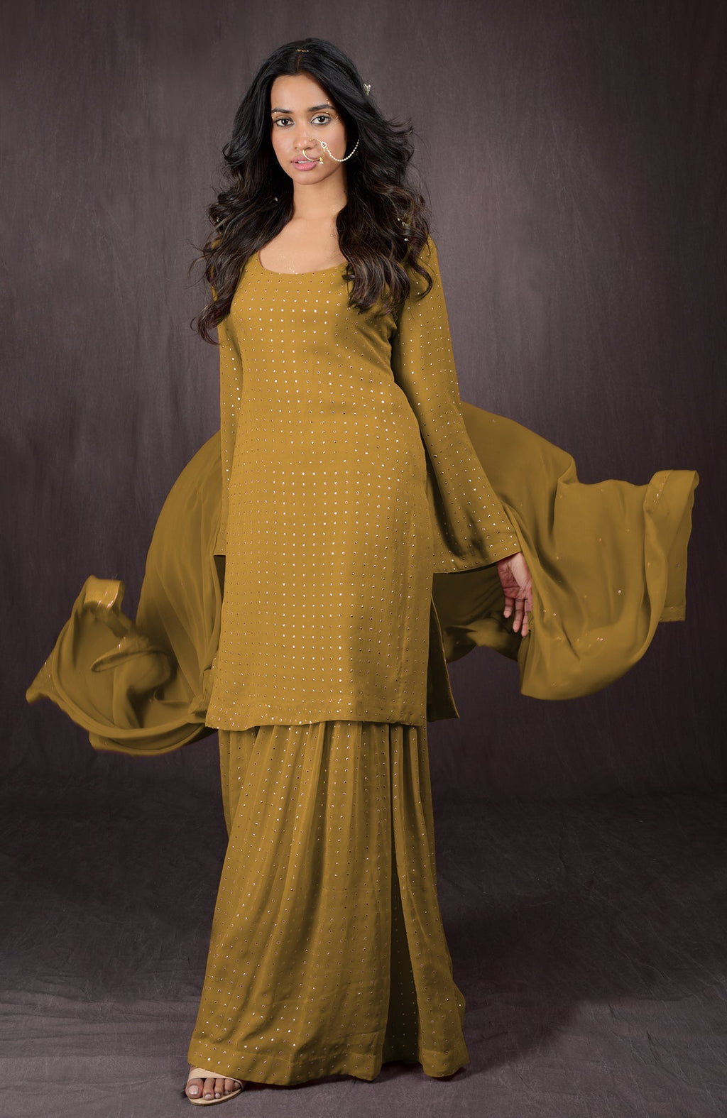 A woman models a mustard yellow sharara set with gold embellishments.