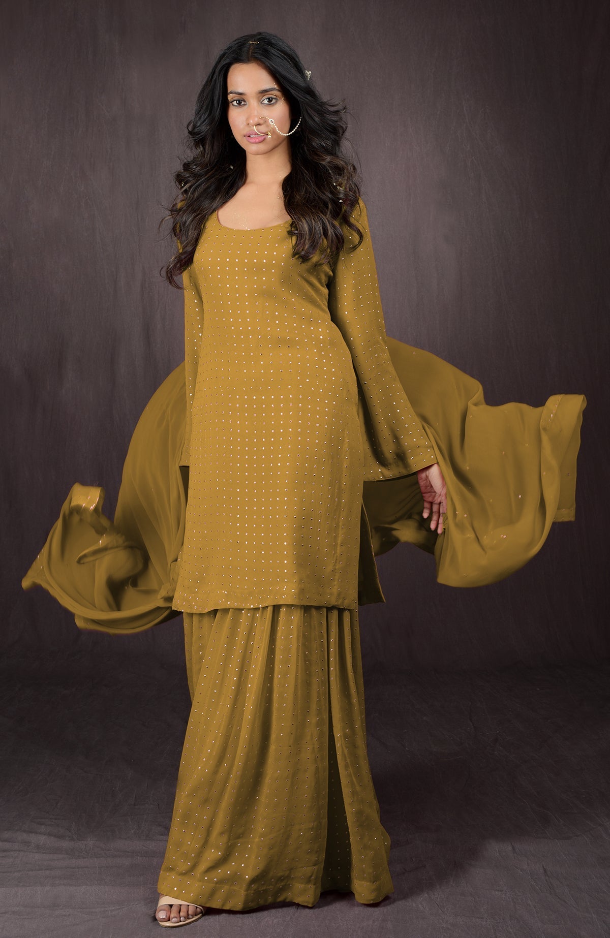 A woman models a mustard yellow sharara set with gold embellishments.
