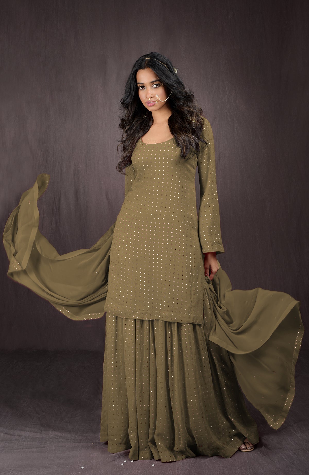 An Indian woman models an olive green sharara set with gold embellishments.