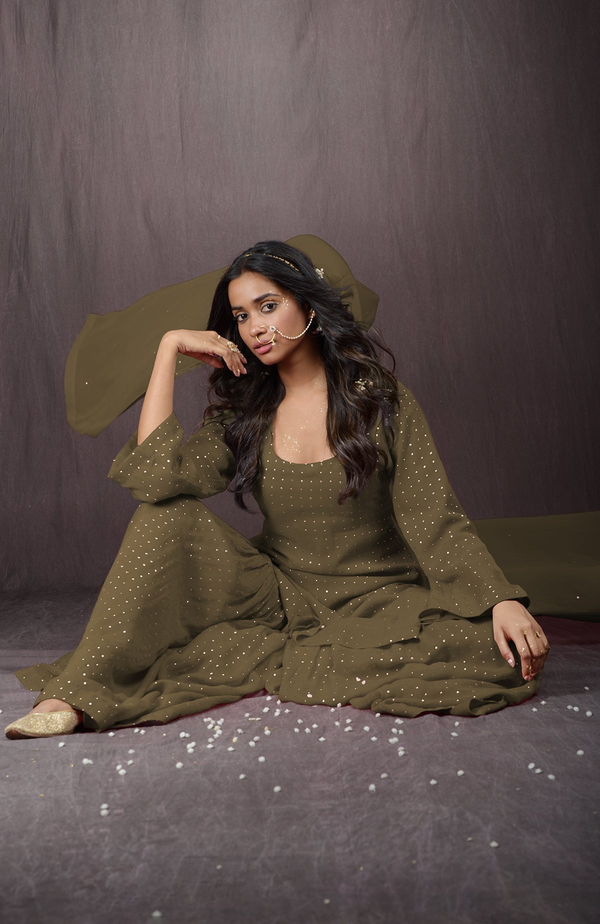 An Indian woman models an olive green sharara set with gold embellishments.
