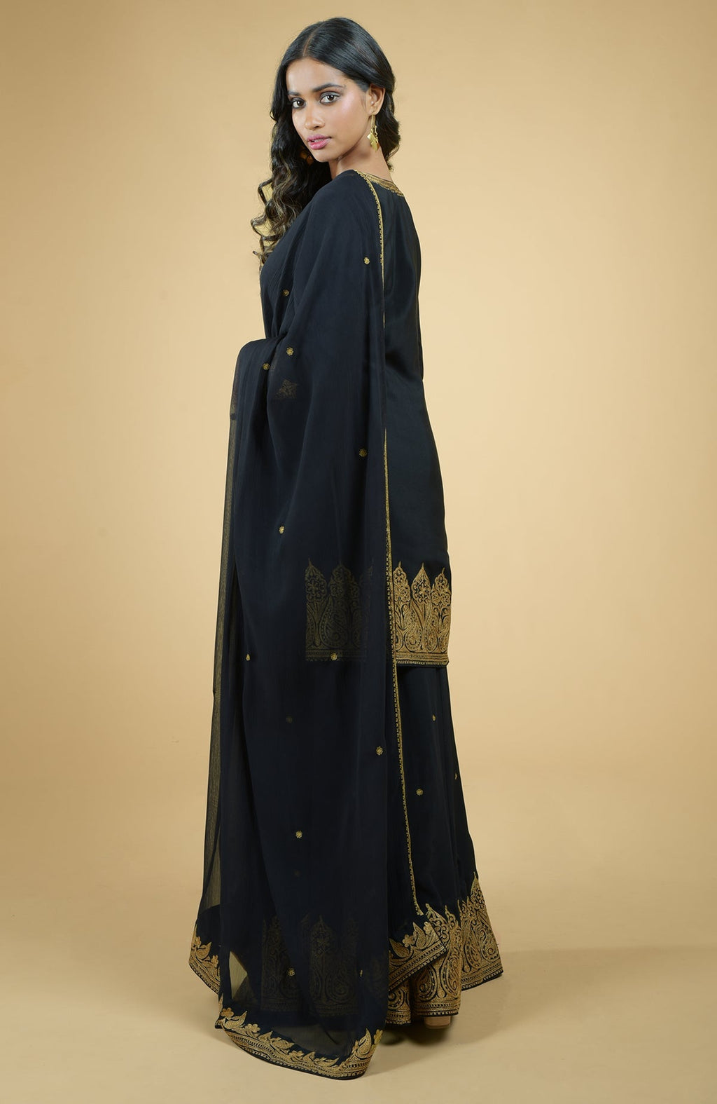 Black sharara set with gold Kashmiri Tilla Aari floral and paisley embroidery and chiffon dupatta.