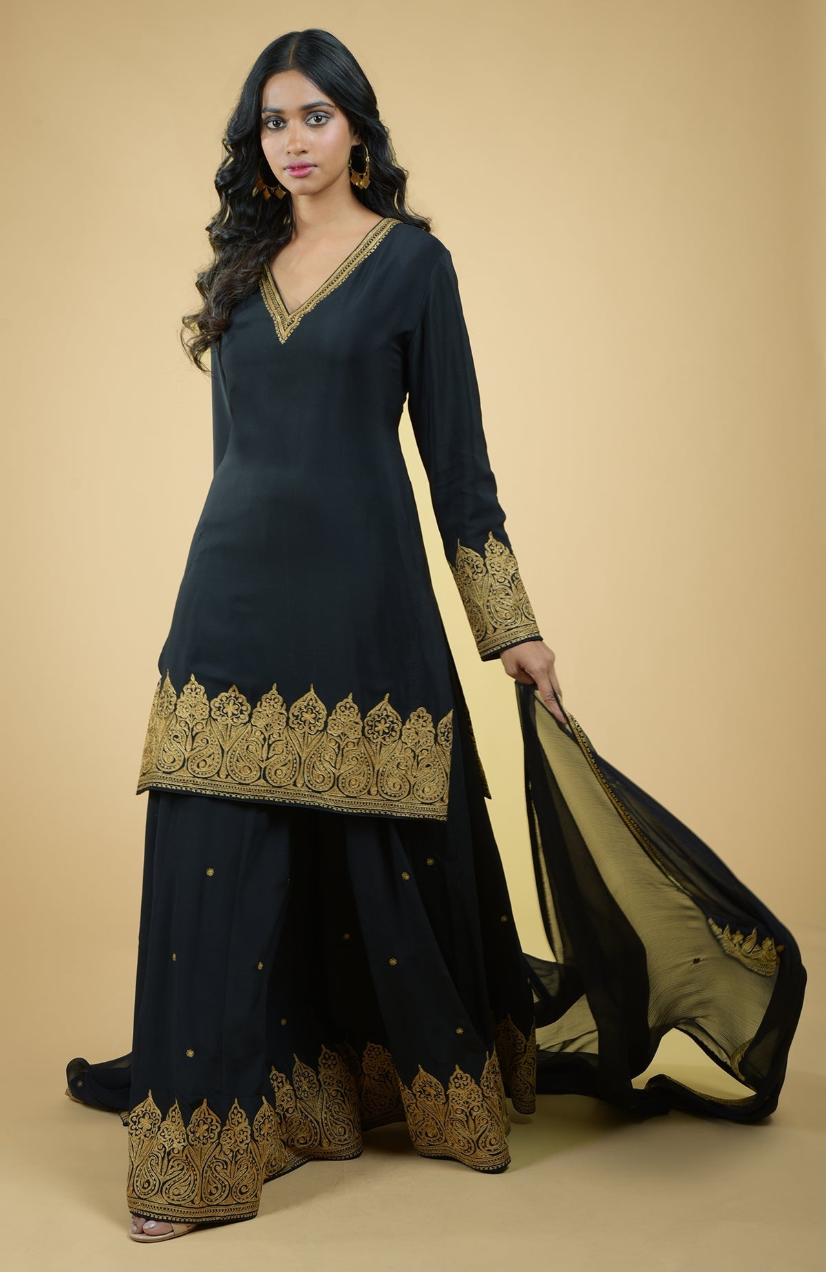 Black sharara set with gold Kashmiri Tilla Aari floral and paisley embroidery and chiffon dupatta.