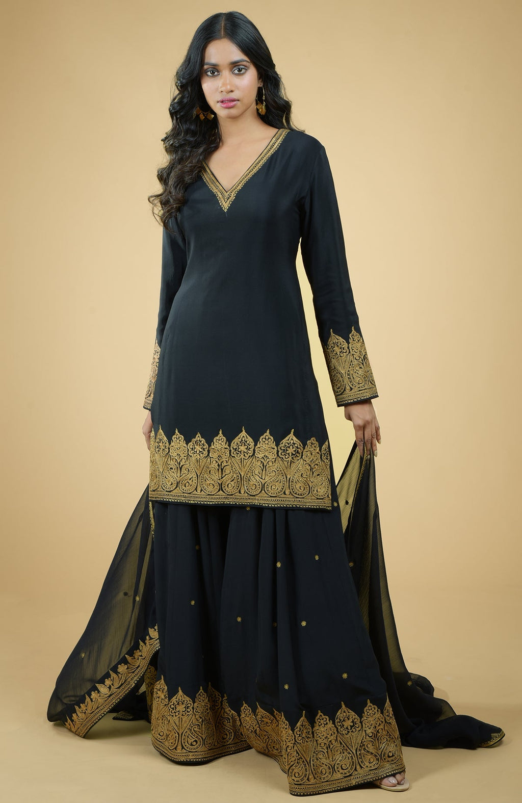 Black sharara set with gold Kashmiri tilla aari floral and paisley embroidery on kurta and dupatta.