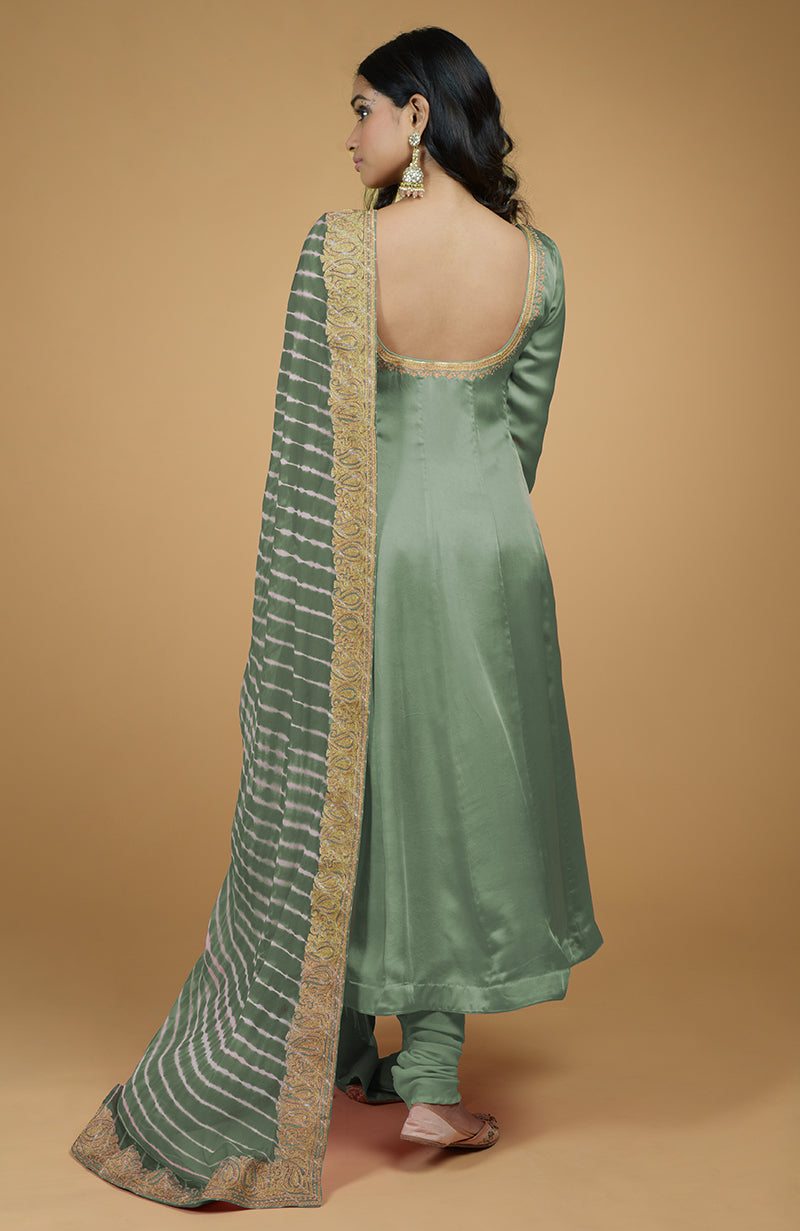 A woman models a jade green Anarkali suit with a striped dupatta and gold embroidery.
