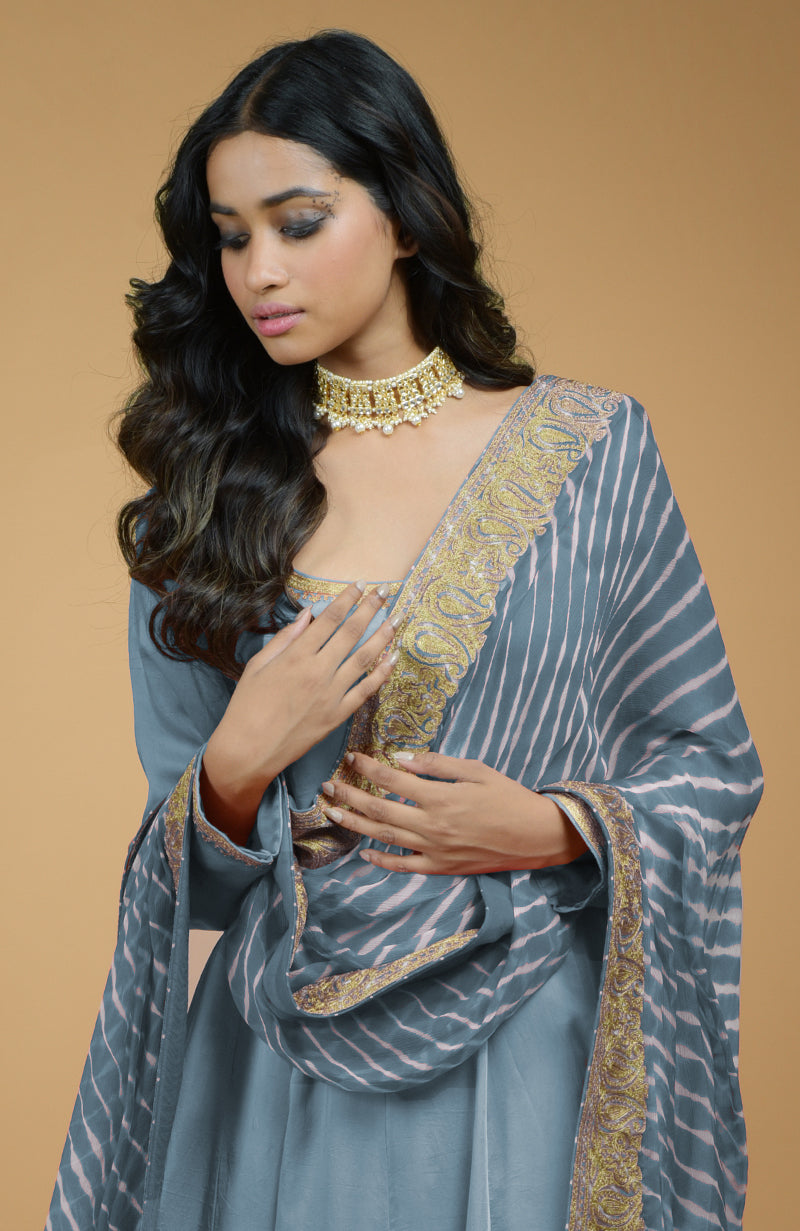 A woman models a greyish blue Anarkali set with a leheriya-tilla embroidered dupatta.