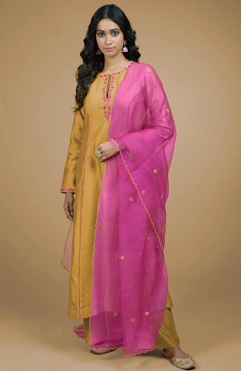 A woman models a mustard kurta set with a magenta organza dupatta.