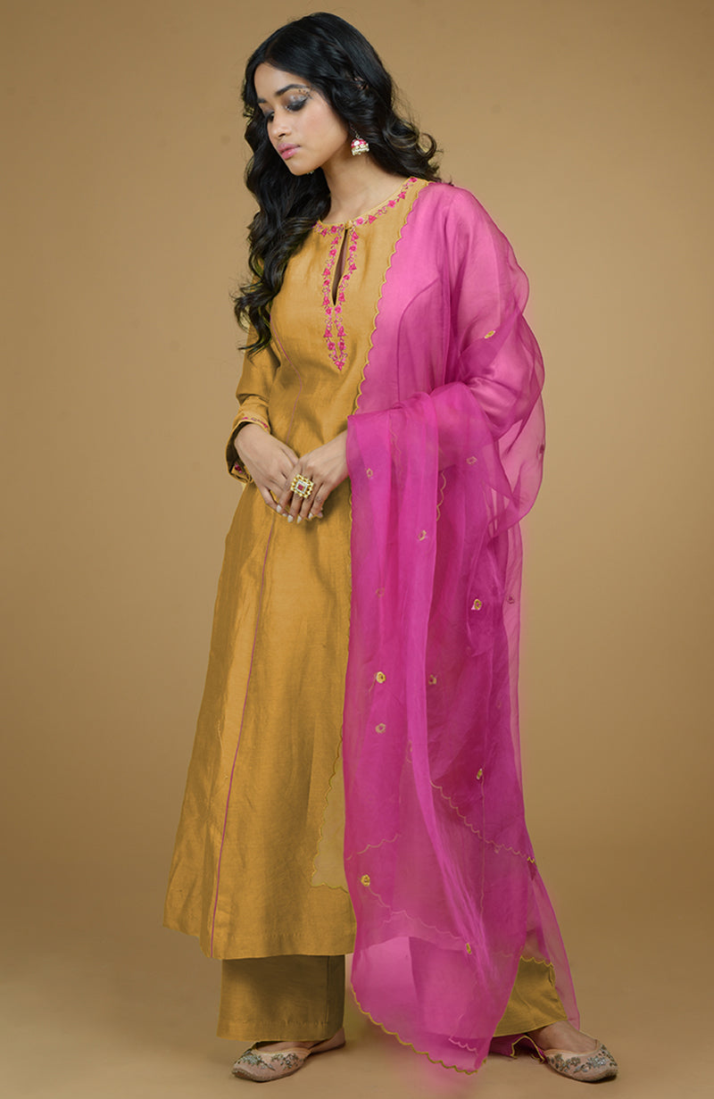 A woman models a mustard kurta set with a magenta organza dupatta.
