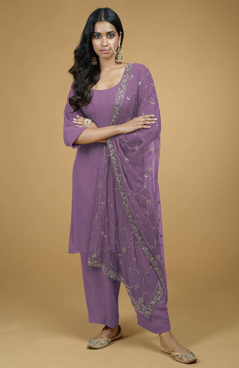 A woman models a purple kurta set with silver embroidery and a matching dupatta.