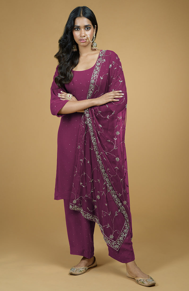 A woman models a peacock pink kurta set with silver embroidery and a matching dupatta.