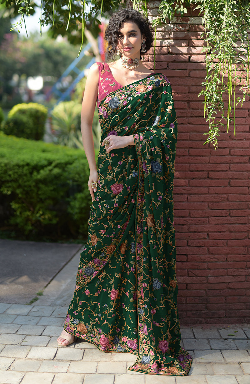 A woman in a dark green floral embroidered saree with a pink blouse.