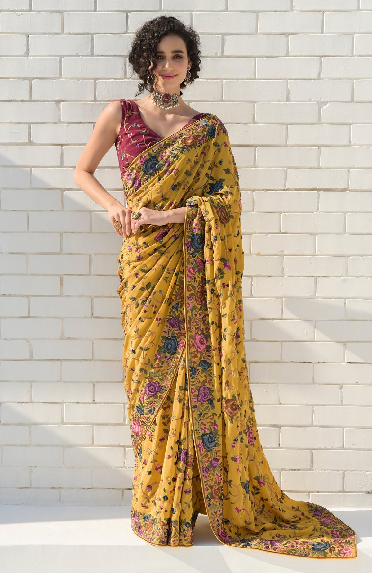 A woman models a beige floral Parsi Gara hand-embroidered saree with a wine blouse.