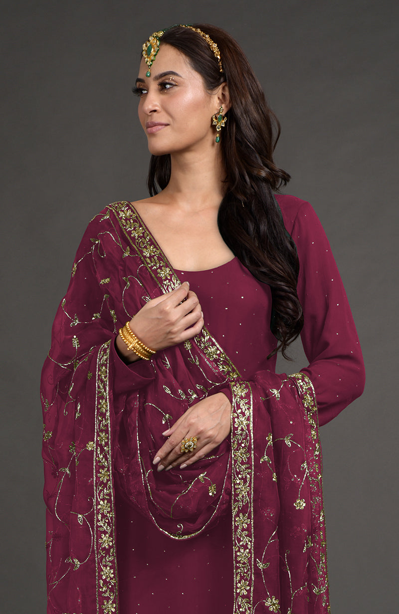 A woman models a wine-colored kurta set with gold embroidery and a matching dupatta.
