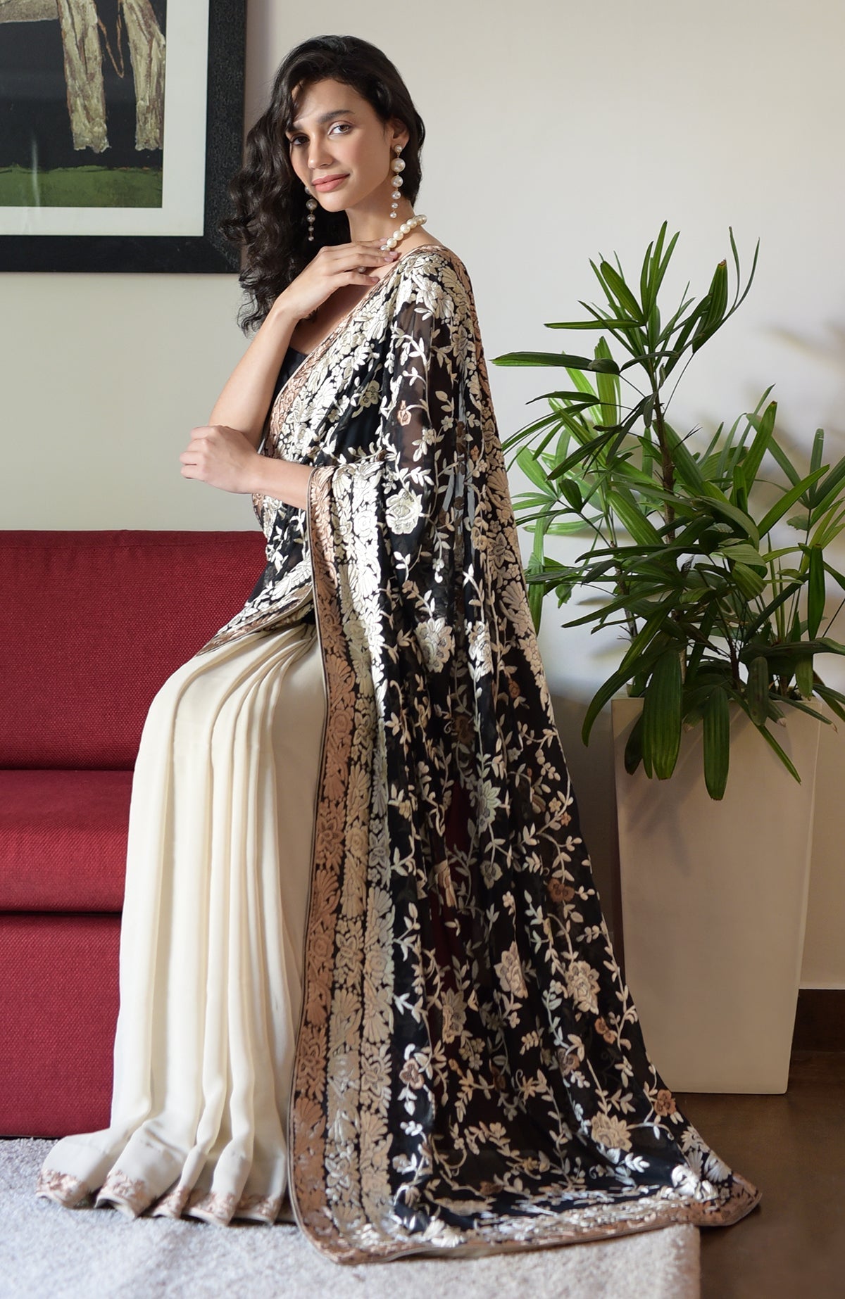 Woman in a black and cream embroidered saree with a pearl necklace and earrings.
