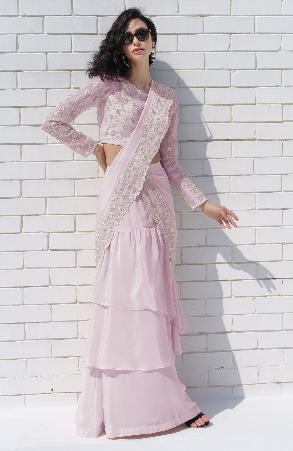 A woman in a lilac silver embroidered draped saree set with sunglasses.
