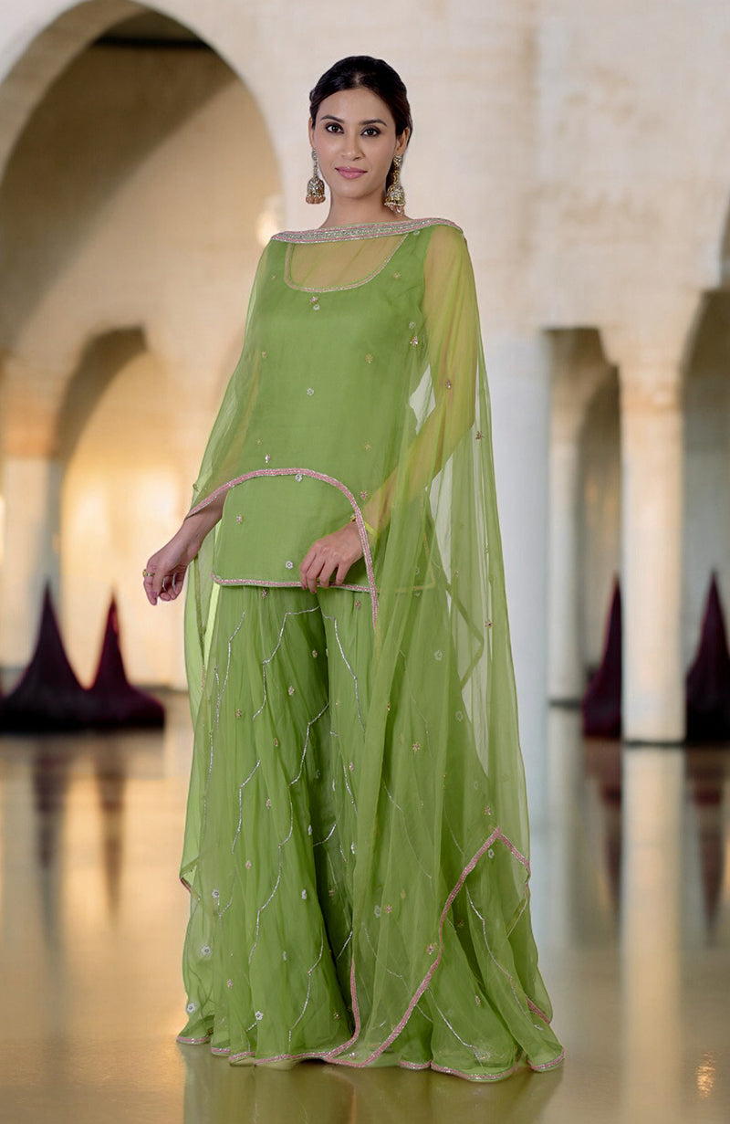 A woman models a lime green hand-embroidered sharara cape set with silver and pink details.