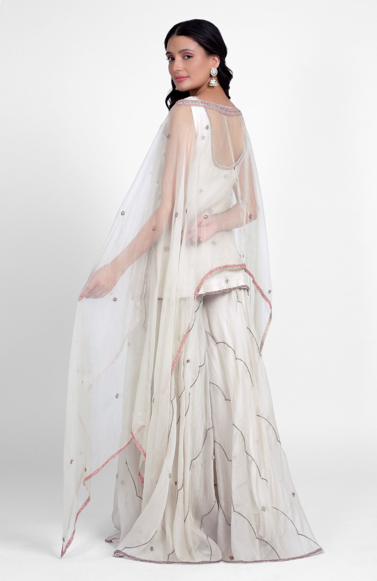 Off-white silk organza sharara set with pastel embroidery, scoop neck kurta, and cape dupatta.