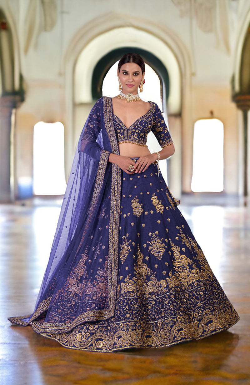 A woman models a blue lehenga set with gold embroidery and a sheer dupatta.