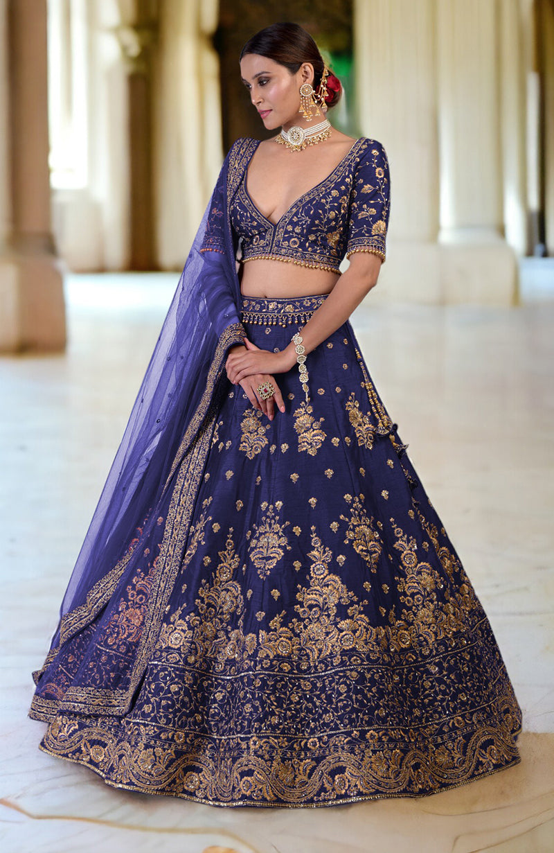 A model wears a plum lehenga set with gold embroidery and a sheer dupatta.
