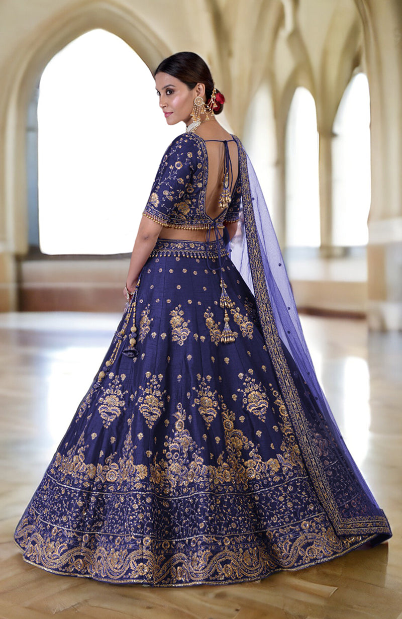 A woman models a blue lehenga set with gold embroidery and a sheer dupatta.