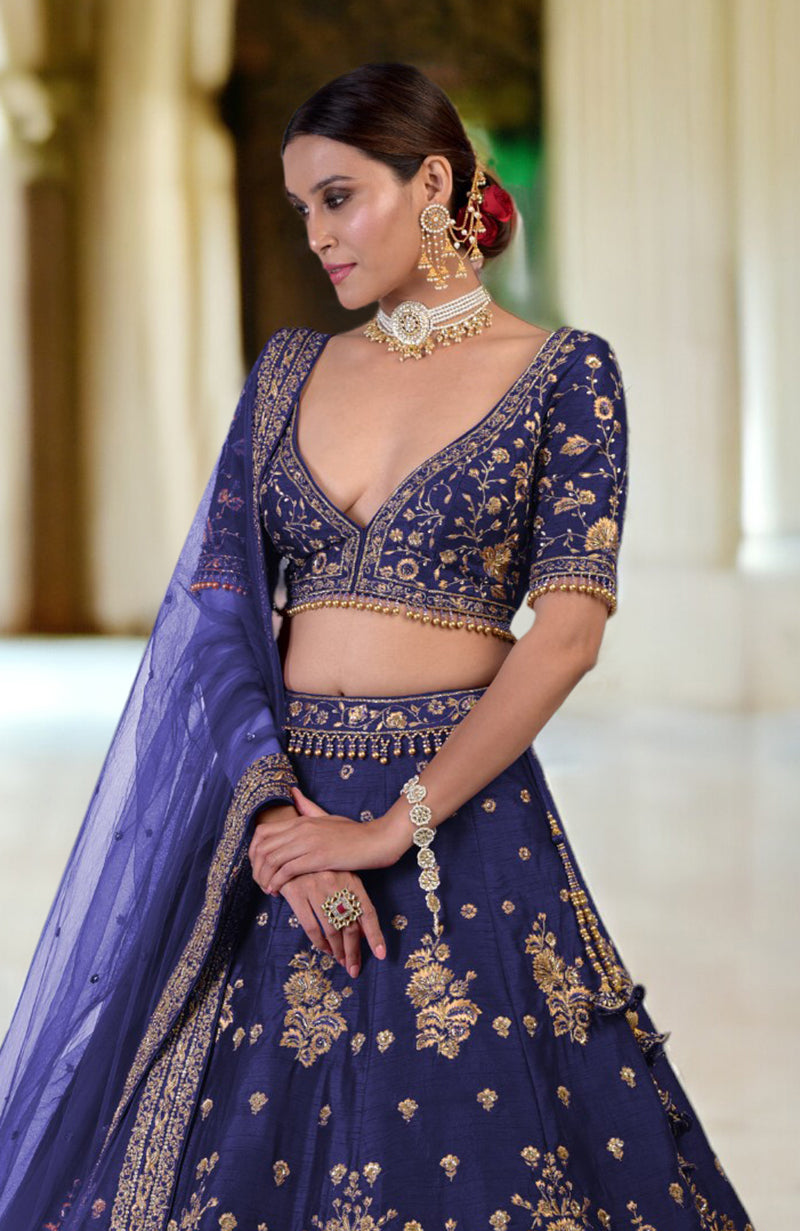A woman models a blue lehenga set with gold embroidery and traditional jewelry.