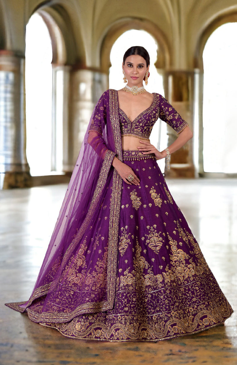 A model poses in a plum lehenga set with intricate gold embroidery and a sheer dupatta.