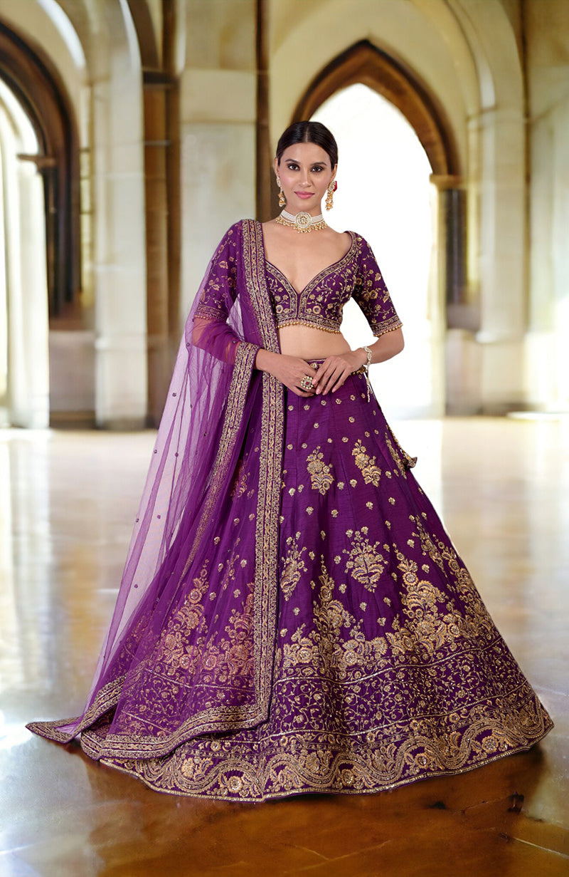 A woman models a plum lehenga set with gold embroidery and a sheer dupatta.