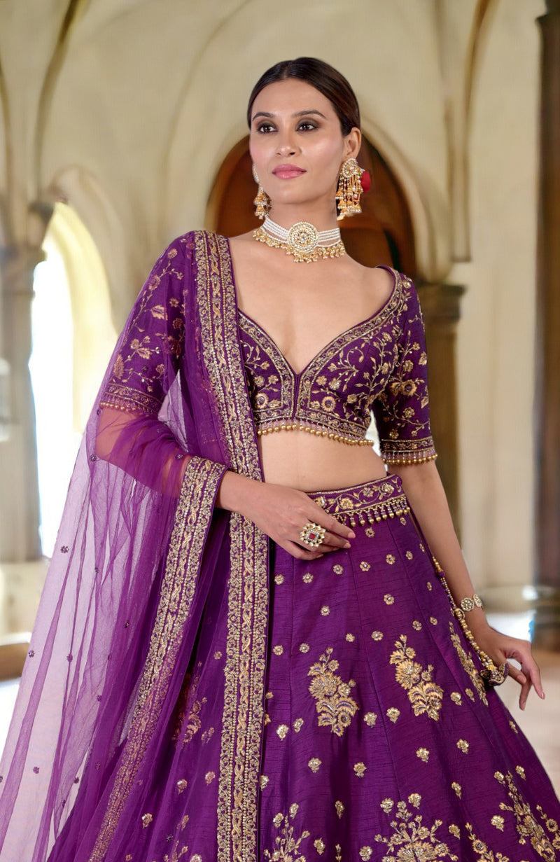 A woman models a plum lehenga set with gold embroidery and a matching dupatta.