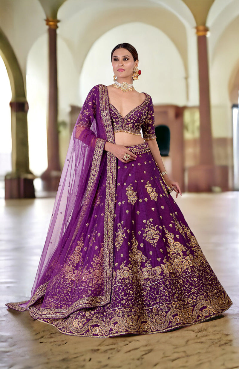 A woman models a plum lehenga set with gold embroidery and a sheer dupatta.
