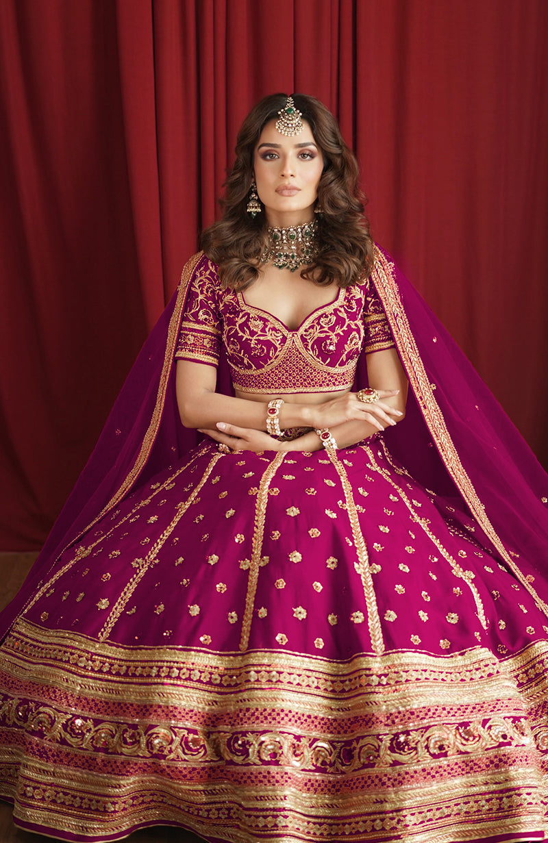 A woman models a boysenberry lehenga set with gold embroidery and a matching dupatta.