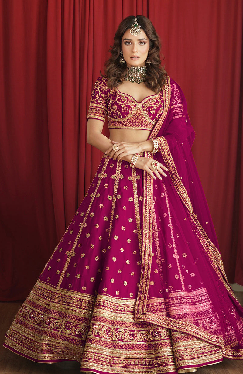 A woman models a boysenberry lehenga set with gold embroidery and a matching dupatta.